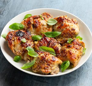 A white plate with glazed chicken pieces garnished with fresh basil leaves.