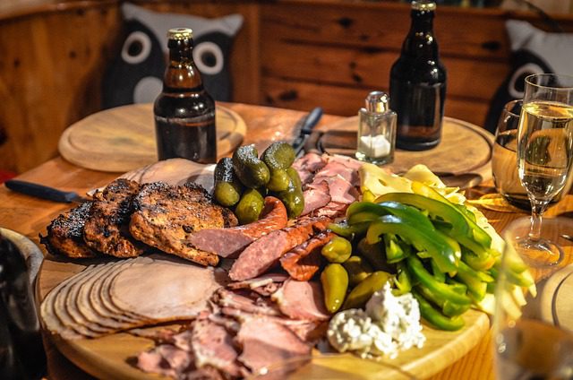 A wooden platter with assorted grilled meats, pickles, and peppers.